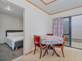 A dining room with a table and chairs and a bed visible in the background at Whangapoua 