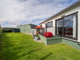 A garden with grass and a deck with a red umbrella at Ducati House - Te anau Holiday Home