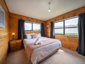A bedroom with a bed and windows at The Back Hut - Te Anau Holiday Home in Te Anau