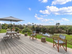 An outdoor deck with a table and chairs overlooking water at Home Away From Home - Ruakaka