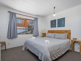 A bedroom with a bed, lamp, chair, and window at Whitianga Holiday Home in Whitianga