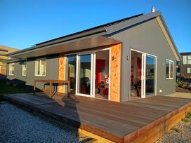A house with a deck and glass doors at Skiwi - Wanaka Holiday Home in Wanaka