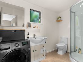 A bathroom with a washing machine, sink, tile floor, and shower at Waipu Holiday Home in Waipu