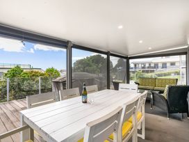 An outdoor patio with a table, chairs, bottle, and couch at Happy Place - Waihi Beach Holiday Home, Waihi Beach