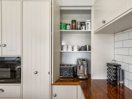 A kitchen with a microwave, toaster, coffee machine, and storage for cups at Sunlit Shores - Papamoa Holiday Homes in Papamoa