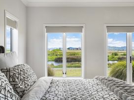 A bedroom with windows overlooking grass and water at Sunlit Shores - Papamoa Holiday Homes, Papamoa