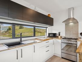 A kitchen with a sink, cabinets, stove, and microwave at Seabreeze Lookout - Moeraki