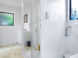 A bathroom with a shower, toilet, and vanity sink at Tides and Time Bach - Ahipara Holiday Home Kaitaia