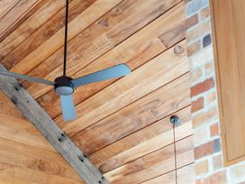 A ceiling fan with a wooden ceiling and brick wall at Mangawhai Heads