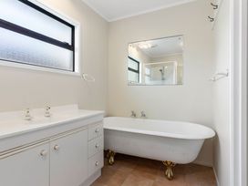 A bathroom with a bathtub, vanity sink, and mirror at Whangamata
