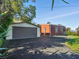 A house and garage in front of a grassy area at Maison Pierre Rouge - Duvauchelle Holiday Home Akaroa