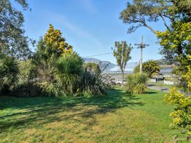 A garden with grass, trees, and water view at Maison Pierre Rouge - Duvauchelle Holiday Home, Akaroa