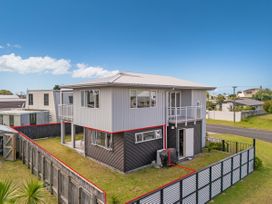 An outdoor view of a two-story house with a balcony and fenced yard at Whangamata Holiday Unit in Whangamata