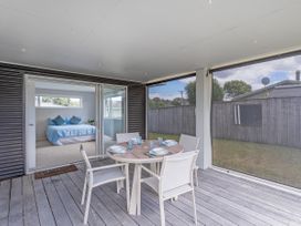 A veranda with a dining table and chairs overlooking a bedroom at Whangamata Holiday Unit in Whangamata