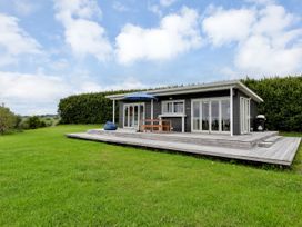 A cabin with a deck and outdoor furniture at Mangawhai Holiday Unit in Kaiwaka
