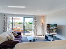A living room with a sofa, television, and a sliding door to an outdoor area at SeaRenity - Waimarama Holiday Home Havelock North