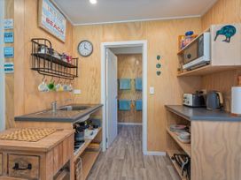 A kitchen with a sink, microwave and shelves at River Cottage - Whitianga Holiday Home in Whitianga