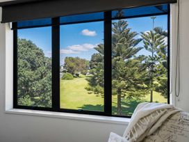 A view of trees and grass through a window in a living room at Mount Maunganui