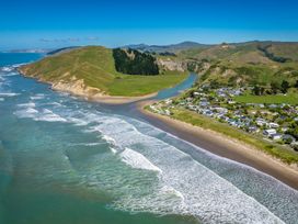 A beach with ocean waves and houses near a river at Pacific Vista - Hawkes Bay in Havelock North