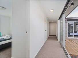 A hallway with doors leading to rooms and windows to an outdoor area at Sweet As on Aquila - Whitianga