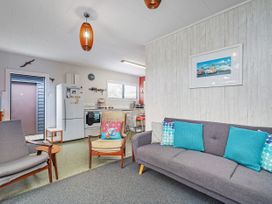 A living room with a sofa, chairs, and kitchen appliances at The Schieck Shack - Whitianga