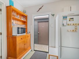 A kitchen with a cupboard a microwave and a refrigerator at The Schieck Shack - Whitianga