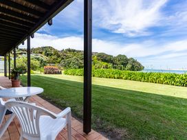 A table and chair on a veranda overlooking grass and the sea at Mangawhai Marvel - Mangawhai Heads