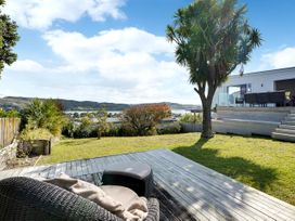 A garden with a tree and deck near water at Raglan Holiday Home