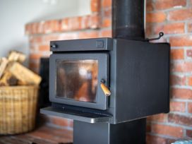 A wood stove next to a basket of logs in a living room at Darling on Dorizac - Te Anau