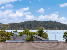 A view of water and hills with buildings and a satellite dish at Raglan Holiday Home in Raglan