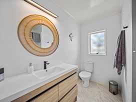 A bathroom with sink, toilet, and mirror at Raglan Holiday Home in Raglan