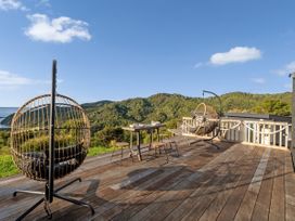 A deck with hanging chairs and a table overlooking the sea and mountains at Little Tui Ridge - Coromandel Holiday Home, Coromandel