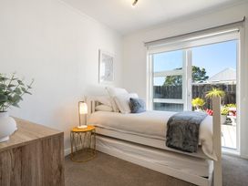 A bedroom with a bed and window opening to outdoor plants at The Wallnutt Grove - Waihi Beach