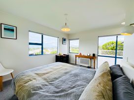A bedroom with a bed and windows at La Maison Bleu - Mangawhai Heads Holiday Home Mangawhai