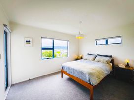 A bedroom with a bed and large windows at La Maison Bleu - Mangawhai Heads Holiday Home Mangawhai
