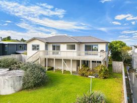 A house with a deck and grass in front at La Maison Bleu - Mangawhai Heads Holiday Home, Mangawhai