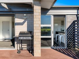 An outdoor area with a barbecue grill and doors to an interior kitchen at Sun & Surf Stay - Papamoa Holiday Home