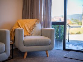 An armchair with a blanket and curtains in a living room at Mustering - Te Anau Holiday Home Te Anau