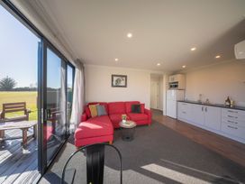 A living room with a red sofa and kitchen appliances at Dusky Rugby Unit - Te Anau Holiday Home Te Anau