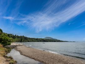 A sandy shore next to a lake with trees in the background at Hauraki Haven - Lake Taupo Holiday Home Pukawa