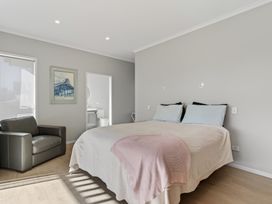 A bedroom with a bed and chair at Mangawhai Holiday Home in Mangawhai