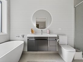 A bathroom with a bathtub, sink, toilet, and mirror at Mangawhai Holiday Home in Mangawhai