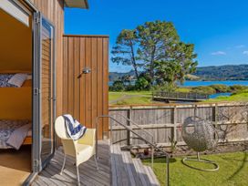 A deck area with a chair and a view of trees and water at Ocean Breeze Family Haven - Pauanui