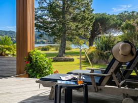 A deck with a chair, table, and views of trees and water at Ocean Breeze Family Haven - Pauanui