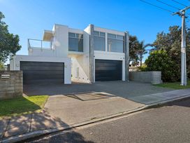 A house with two garage doors and a balcony at Sandbanks, Papamoa Holiday Home, Papamoa