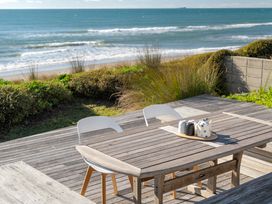 An outdoor dining setup with a table and chairs overlooking the ocean at Sandbanks, Papamoa Holiday Home, Papamoa