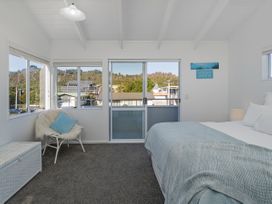 A bedroom with a bed, windows, and a chair at Whangamata Holiday Home in Whangamata