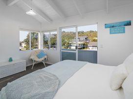 A bedroom with a bed and large windows at Whangamata Holiday Home in Whangamata