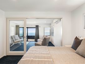 A bedroom with a bed and chairs visible through a glass door at Sunbrae Sands - Mount Maunganui Holiday Homes, Mount Maunganui