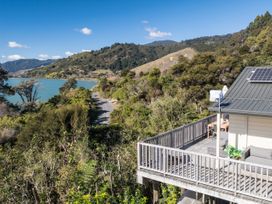 An outdoor deck with a table and chairs overlooking water and mountains at Tepuia Cottage - Havelock Holiday Retreat Marlborough